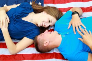 La nota trata sobre el proceso de obtención de la visa de prometido en Estados Unidos. La foto muestra una pareja con la bandera de este país.