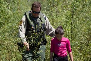 Nota informando sobre las novedades respecto al programa Permanecer en México. La foto es de un agente de la Patrulla Fronteriza junto a una niña migrante.