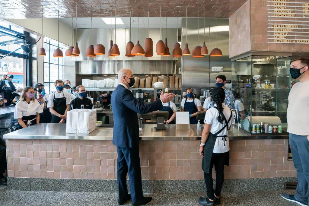 Nota sobre la reforma migratoria 2021 y su vínculo con la falta de mano de obra en los Estados Unidos. La imagen es del presidente Biden junto a trabajadores de una cafetería.