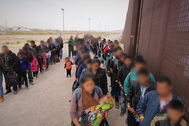 Nota proporcionando las últimas noticias de inmigración hoy que anuncian un control de inteligencia por parte del DHS para frenar la caravana de migrantes. La imagen es de personas aguardando en la frontera.