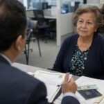 Una mujer latina mayor escucha atentamente a un oficial de USCIS durante su entrevista de naturalización en una oficina federal de Estados Unidos. Ciudadanía sin examen.